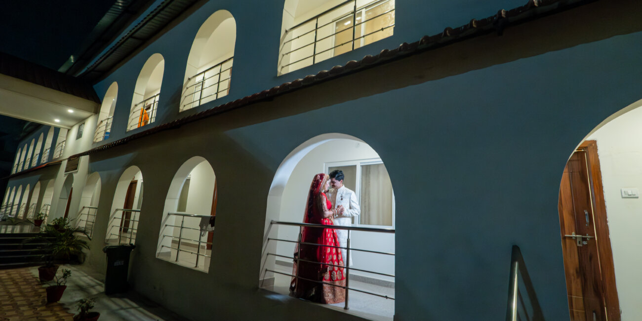 A North Indian bride and groom stand together near a grand building, their attire reflecting tradition and modern elegance.