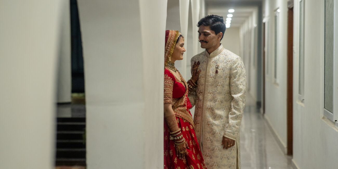 A Indian bride and groom face each other in traditional wedding attire, their eyes locked with love and promise.