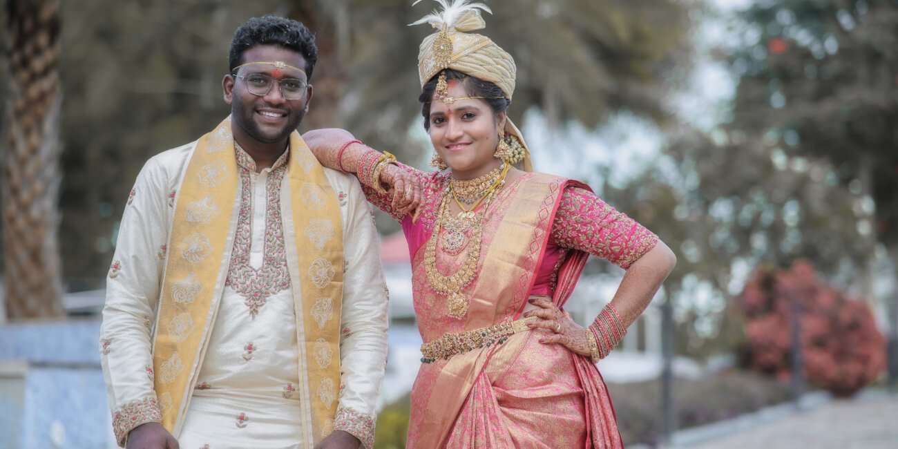 "Telugu bride wearing the groom’s hat and placing her hand on his shoulder while posing for a post-wedding photo"