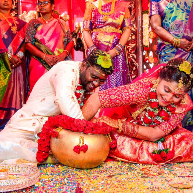 "Telugu bride and groom playfully searching for the ring in a traditional silver vessel filled with water during the post-wedding ritual"