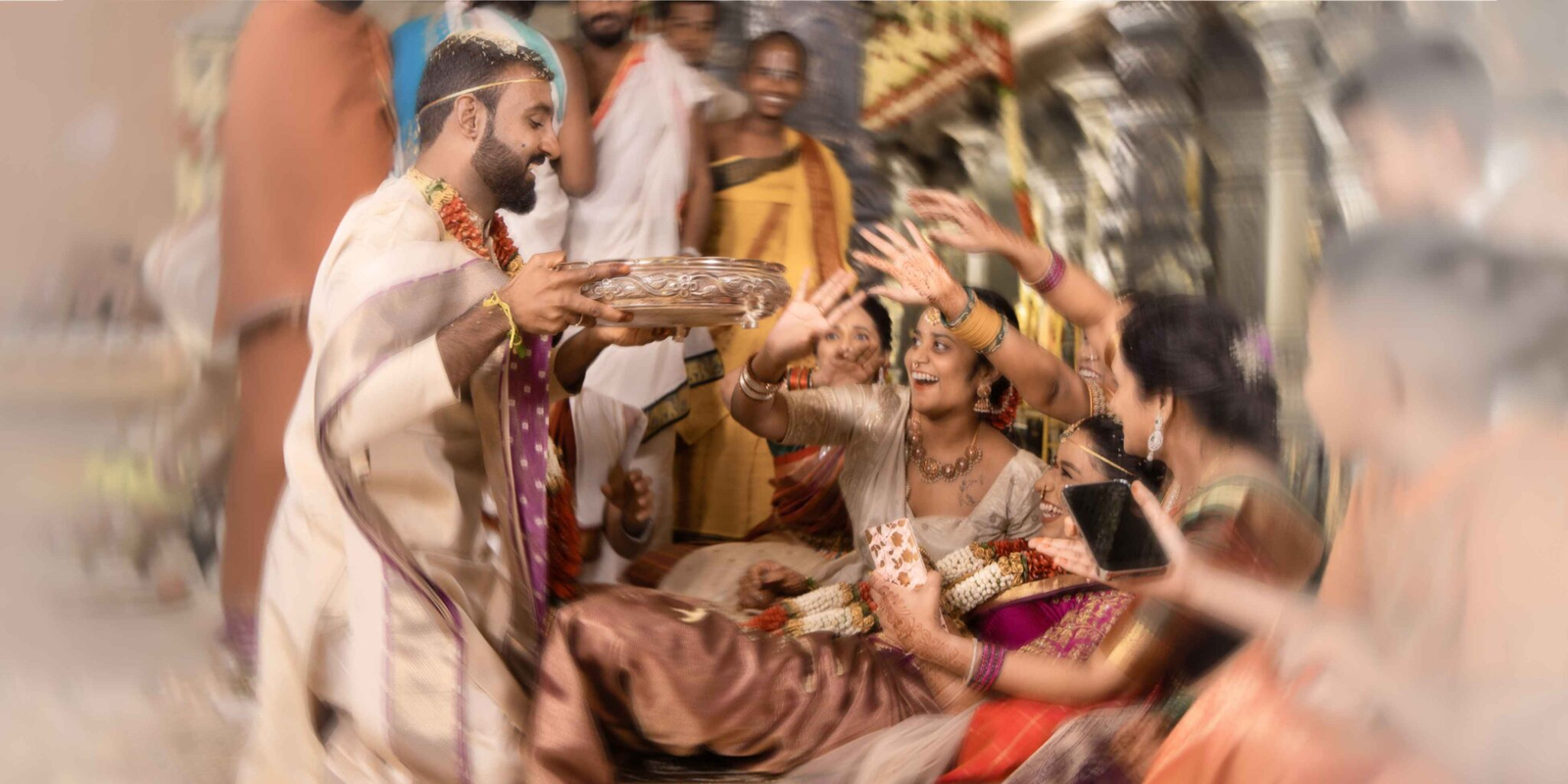 Playful wedding moment where the groom is about to pour thalambaralu on the bride, but her family pulls her back, laughing and enjoying the ritual.