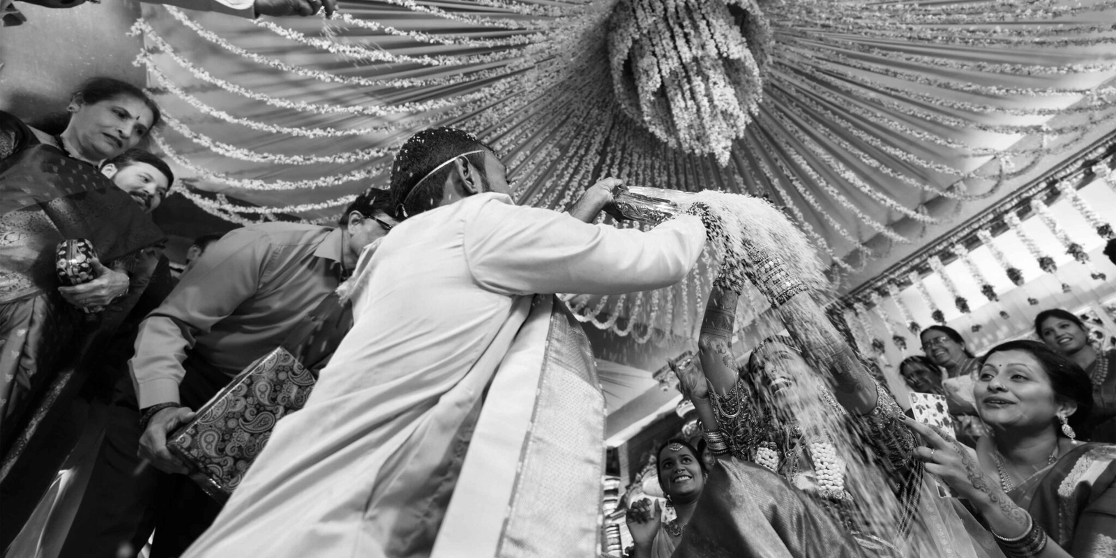 Groom joyfully pouring thalambaralu (sacred rice mixed with turmeric) over the bride’s head during the wedding ceremony, surrounded by smiles and blessings.